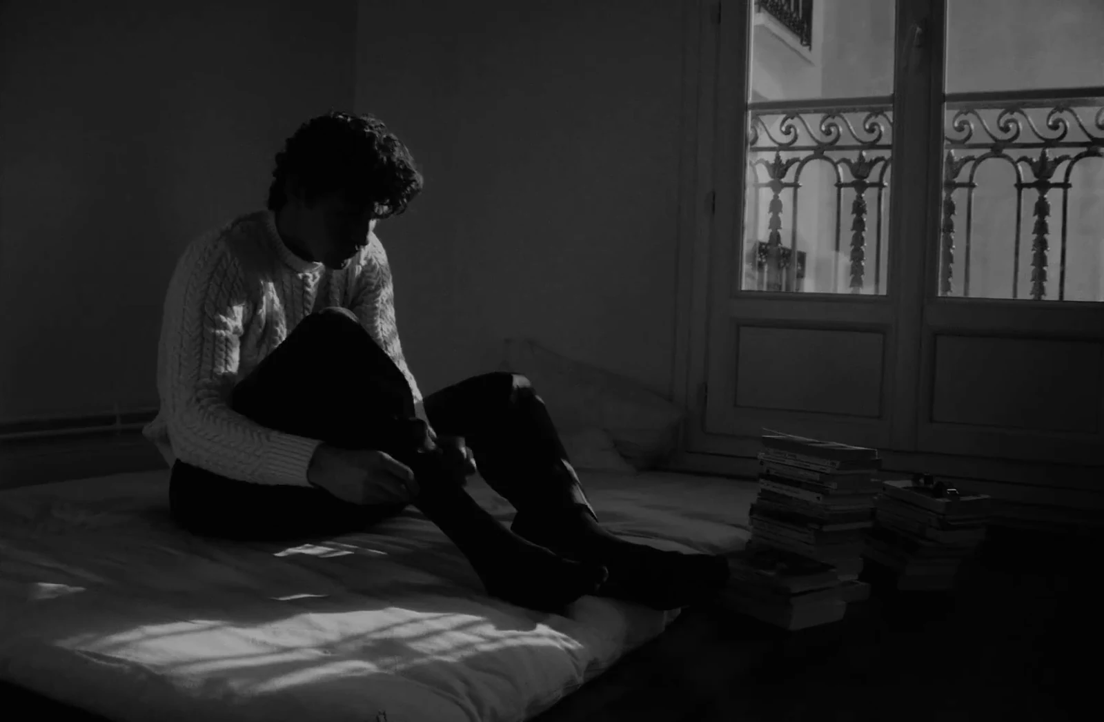 Un homme assis au sol d'une chambre, en noir et blanc